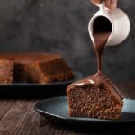 A slice of chocolate cake being drizzled with chocolate sauce