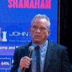 RFK Jr. Exposes Doctor Nutrition Scandal A man speaking into a microphone at an event with a large screen behind him displaying data