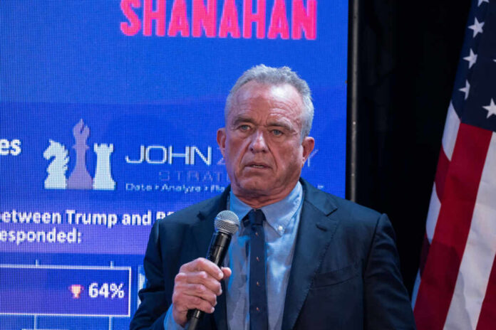 shutterstock2456684663jpg A man speaking into a microphone at an event with a large screen behind him displaying data