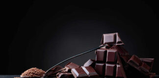 A pile of dark chocolate bars with cocoa powder on a black surface