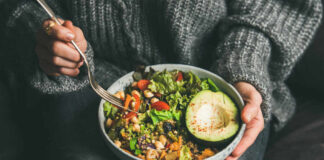 A person holding a bowl of colorful salad with avocado and greens