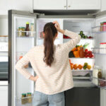 Hidden Mold Dangers in Household Fridges A woman standing in front of an open refrigerator filled with various fruits and vegetables