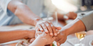 Several hands stacked together over a plate of food, symbolizing unity and support
