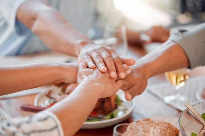 Several hands stacked together over a plate of food, symbolizing unity and support