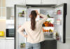 A woman standing in front of an open refrigerator filled with various fruits and vegetables
