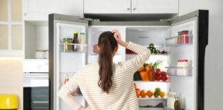A woman standing in front of an open refrigerator filled with various fruits and vegetables