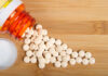 Spilled white pills from a prescription bottle on a wooden surface