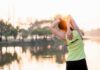 Back Pain? This Simple Move Saves Posture A woman stretching her arms by a lake during sunrise
