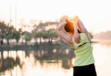Back Pain? This Simple Move Saves Posture A woman stretching her arms by a lake during sunrise