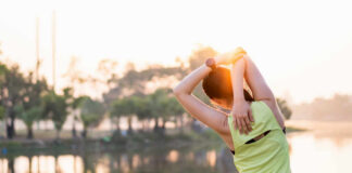 A woman stretching her arms by a lake during sunrise