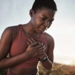 Unlock VO2 Max Gains With Zone Training A woman in athletic wear holding her chest with a pained expression outdoors
