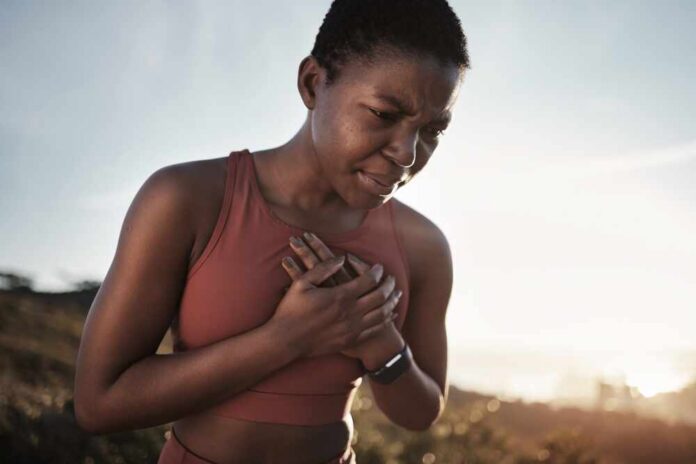 shutterstock_2239940039.jpg A woman in athletic wear holding her chest with a pained expression outdoors