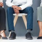 Three individuals in business attire sitting on chairs, showcasing their shoes and legs