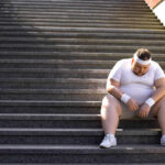 Massive Study REVEALS Exercise Guidelines Failing An exhausted man in sportswear sitting on outdoor stairs, looking down.