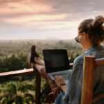 Person working on a laptop outdoors with a scenic sunset view
