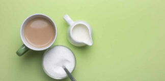 A cup of coffee, a bowl of sugar, and a creamer on a green background