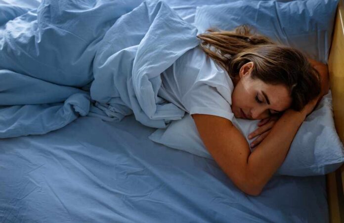 A woman sleeping peacefully on a bed with blue sheets