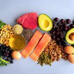 Mediterranean Diet : Aging Hack or Hype? An assortment of healthy foods including fish, nuts, fruits, and vegetables arranged on a light background