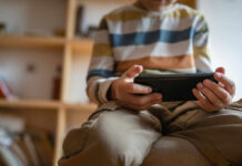 Child sitting on a couch, holding a smartphone and focused on the screen