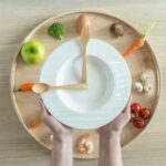 Kitchen Staple Linked To Faster Aging Hands holding a white plate surrounded by fresh vegetables and an egg