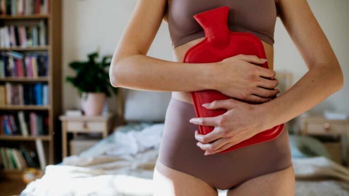 Woman,At,Home,Suffering,From,Menstrual,Pain,,Having,Cramps.,Woman Woman in a cozy bedroom holding a red hot water bottle against her abdomen