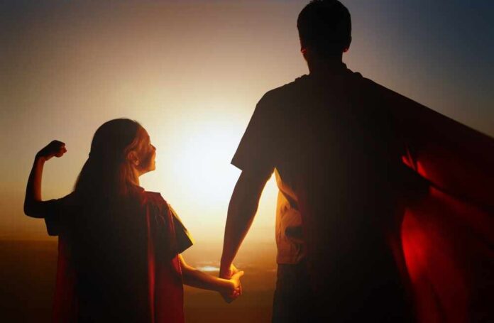 Child and adult in capes holding hands at sunset