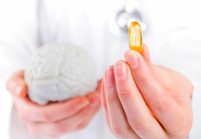 Closeup,Photo,Of,Doctor,Holding,Omega,3,Capsule,In,Hand A medical professional holding a brain model in one hand and a yellow supplement capsule in the other