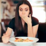 Allergies That Can Kill Woman covering mouth while looking at a plate of pasta