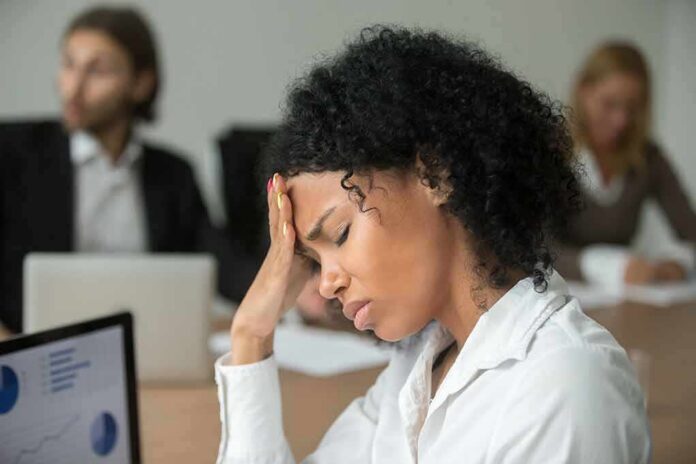 shutterstock_1022439613 Woman in office holding her head with eyes closed