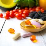 Silent Deficiency Wrecks Mood And Muscles Wooden spoon holding assorted vitamin pills beside fresh fruits and vegetables