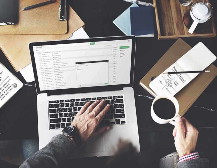 Person working on a laptop with email inbox open and holding a cup of coffee
