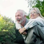 older couple smiling during piggyback ride in a park
