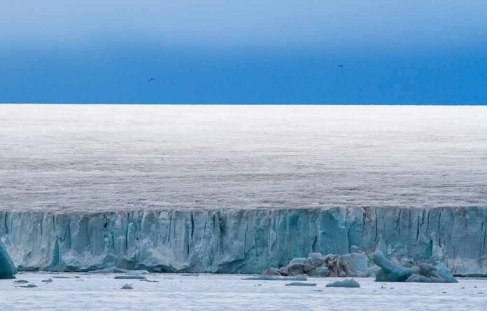 shutterstock_1014335092 Ice cliff along a polar glacier under a blue sky