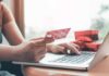 Person holding credit card while typing on laptop