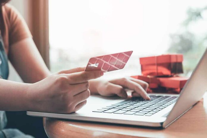 shutterstock_1024357639 Person holding credit card while typing on laptop
