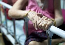 Elderly person’s hands resting on a hospital bed rail