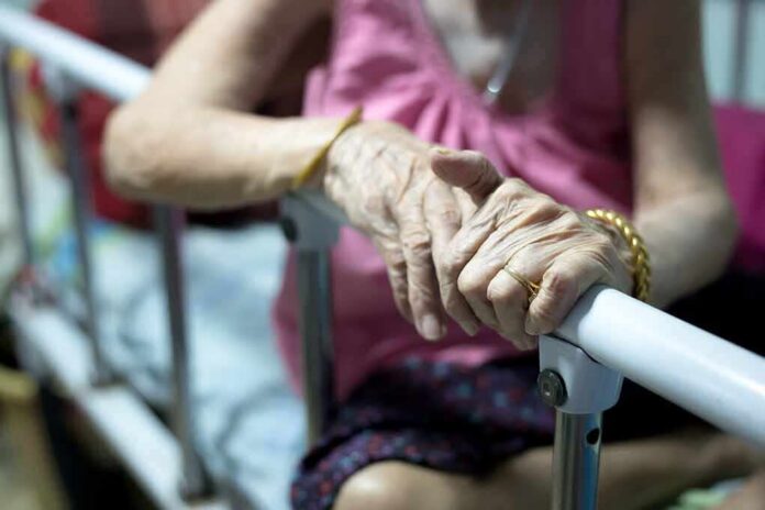 Elderly person’s hands resting on a hospital bed rail