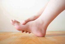 Arthritis Relief Without Surgery Hand holding the arch of a bare foot on a wooden floor