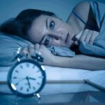 PTSD’s Sleep Trap — Clinicians Break It Woman lying awake in bed beside an alarm clock