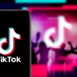 Smartphone showing TikTok logo against neon party silhouettes