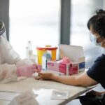 Healthcare worker performs finger-prick test on masked patient