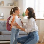 Mother kneels to talk with daughter wearing backpack