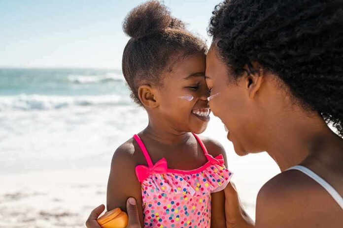 shutterstock_2143243917 Mother and daughter smiling with sunscreen at the beach