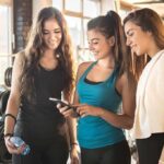 three women in gymwear looking at a smartphone
