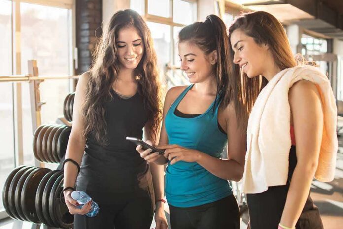 shutterstock_552058372 three women in gymwear looking at a smartphone