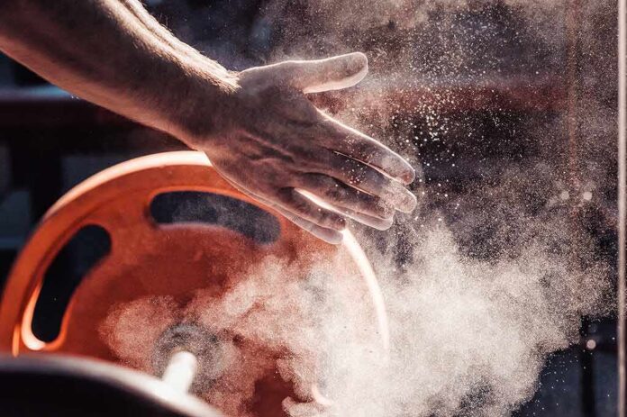 Athlete’s chalked hands above an orange weight plate