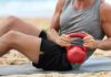 The Ultimate Guide to Body Recomposition Man doing sit-ups with a red kettlebell on a beach mat