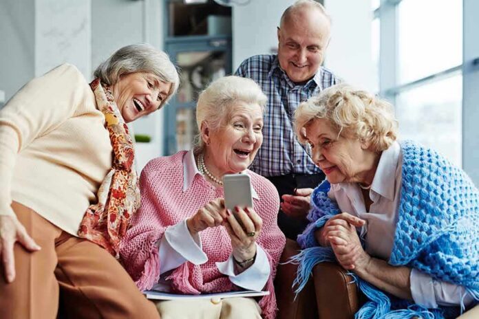 1783879669001-zeia2z-shutterstock-615337679 Group of seniors smiling and looking at a smartphone together