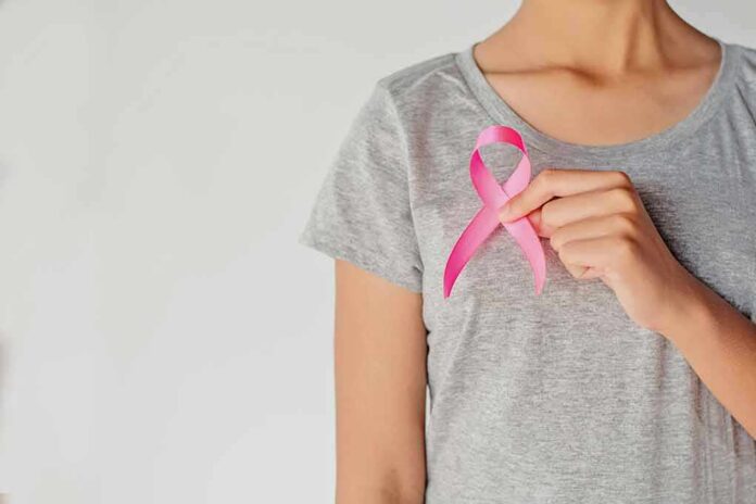 shutterstock_1032241918-1 Person holding a pink ribbon on a gray shirt