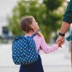 Young girl with polka dot backpack holding adult's hand outdoors